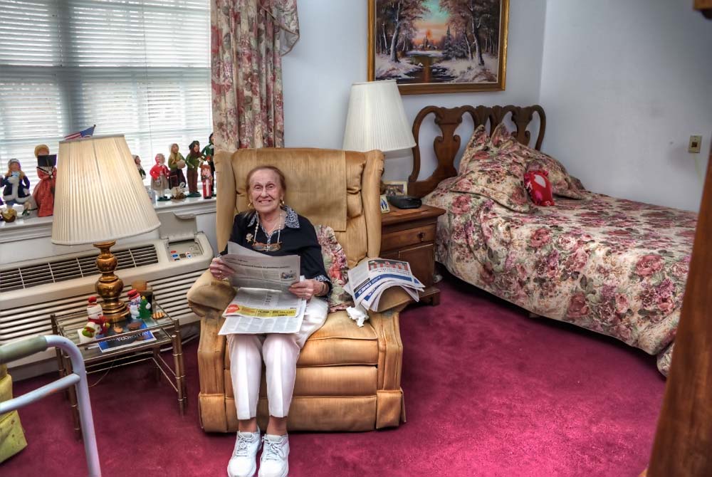 Smiling female resident sitting in her easy chair reading paper